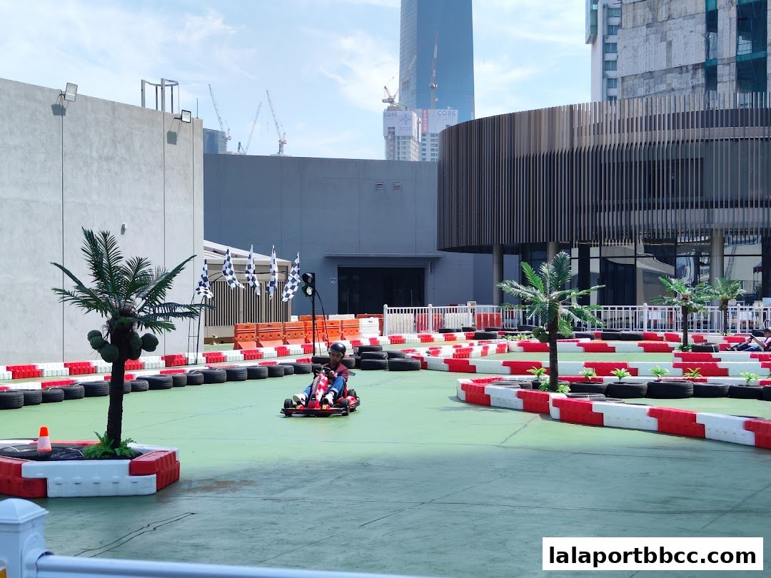 A go-kart track with a person racing, surrounded by tires and palm trees.