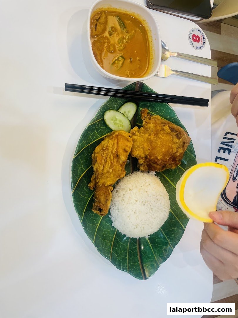 A delicious meal featuring fried chicken, rice, curry, and cucumber slices served on a leaf-shaped plate.