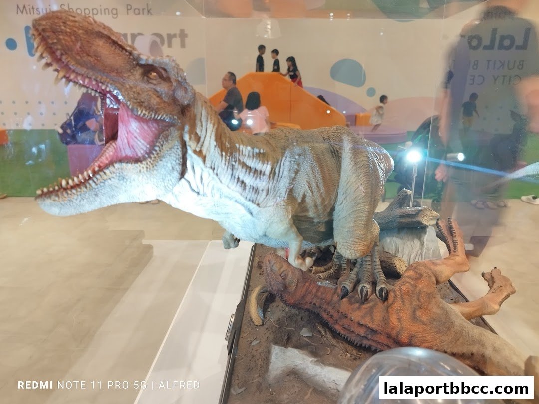 A realistic dinosaur model display with children playing in the background.