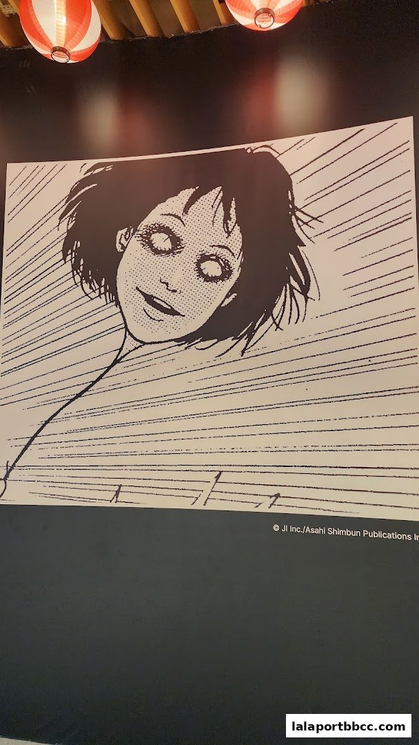 A black and white illustration of a character with wide, staring eyes and a slight smile.
