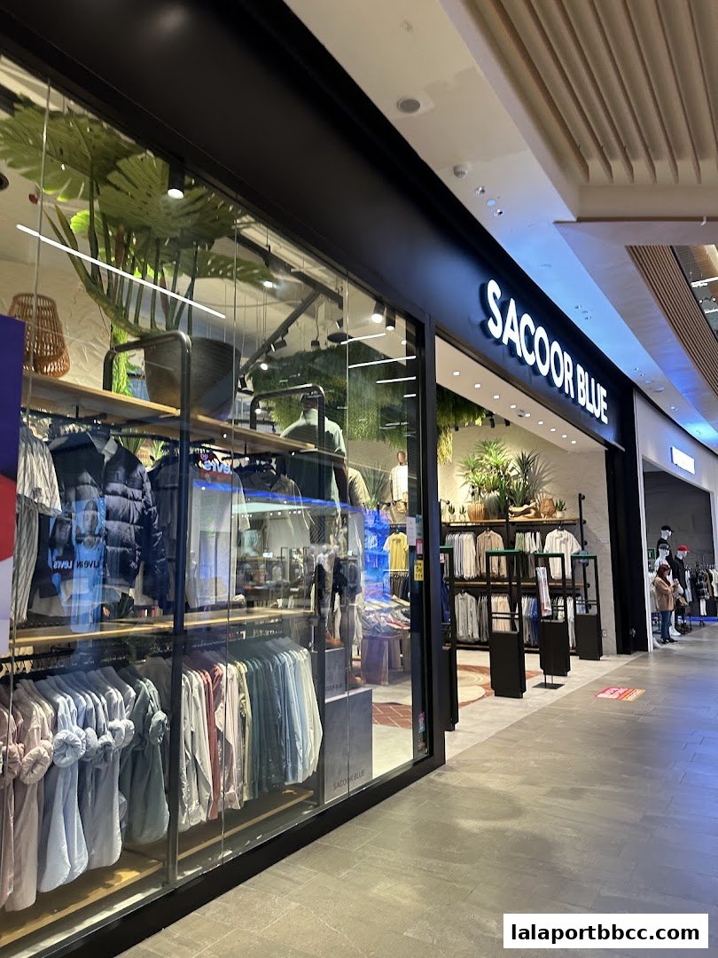 The Sacoor Blue store front displays a variety of clothing on racks and mannequins, with plants adding a decorative touch.