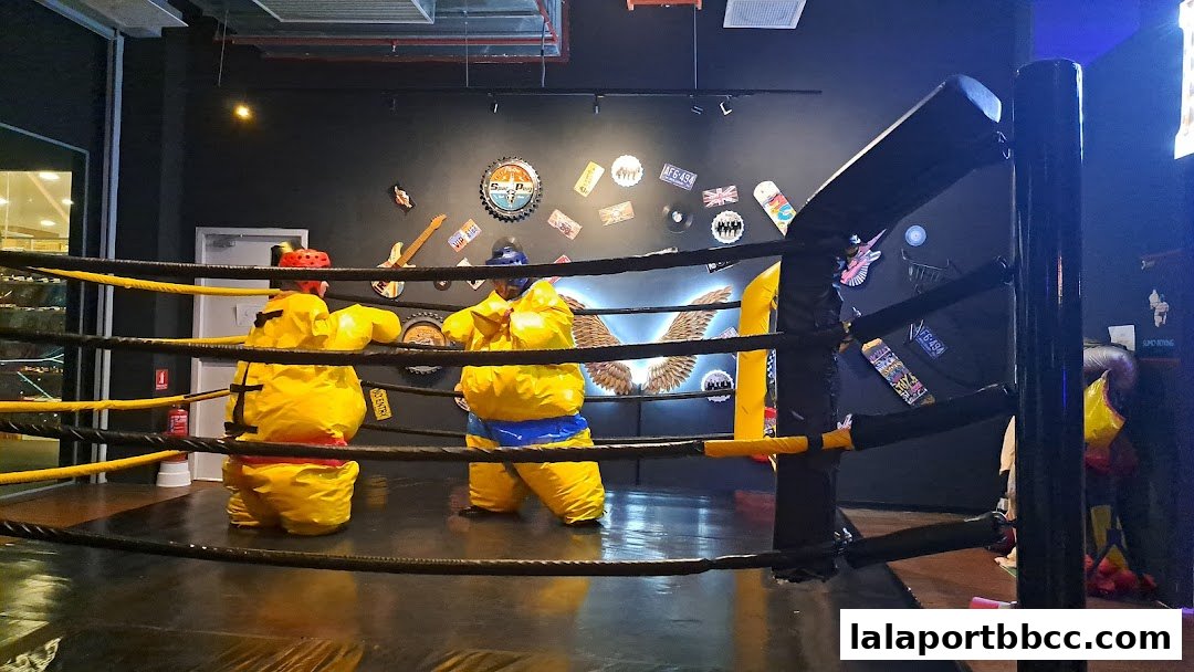 Two people in inflatable sumo suits are playfully sparring inside a boxing ring.