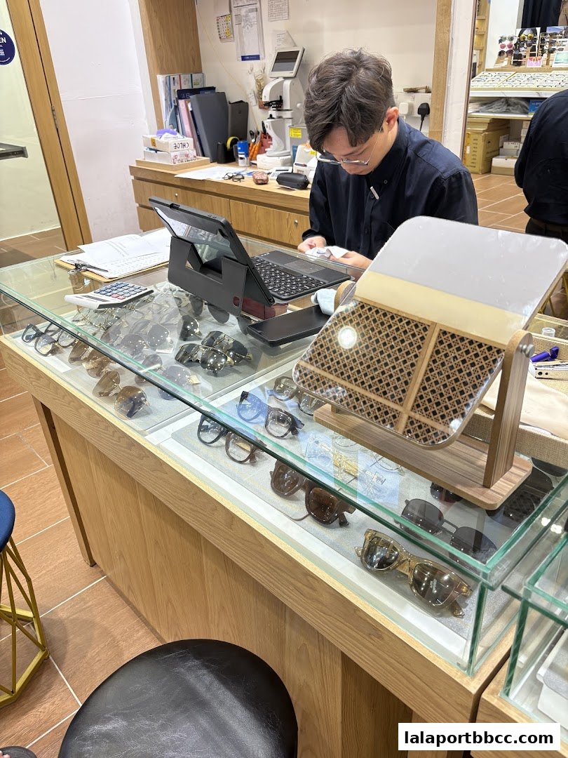 An optician's shop interior with a display of eyeglasses and sunglasses, and an employee at the counter.