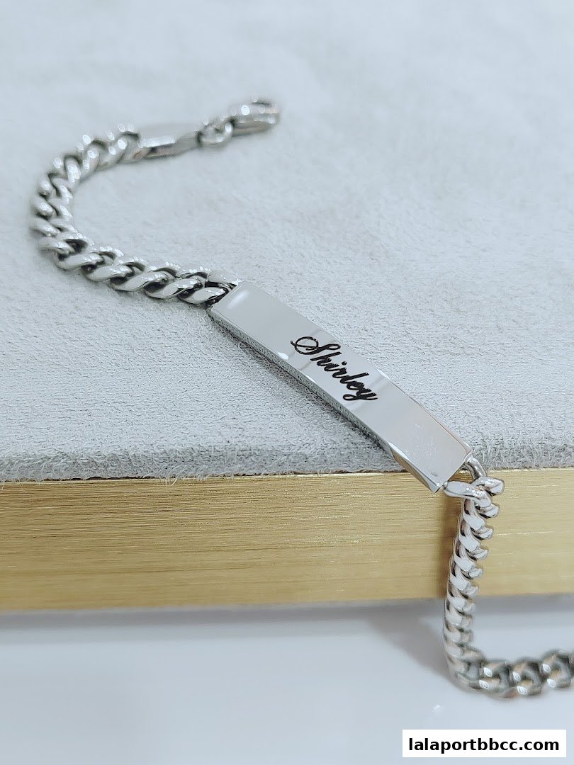 A close-up shot of a silver bracelet with the name 'Shirley' engraved on a rectangular tag.
