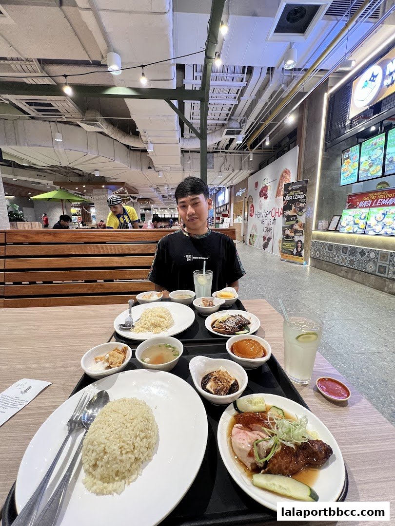 A person sits at a table with a tray of chicken rice and side dishes.