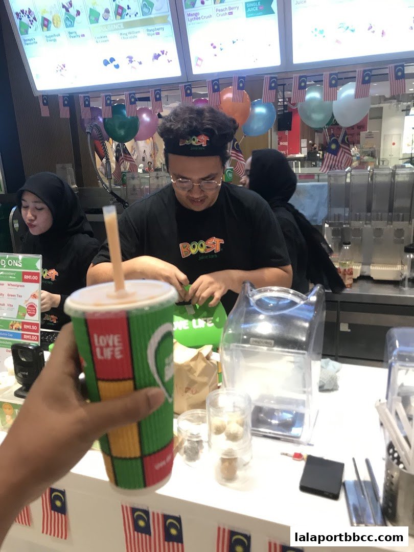 A person holds a Boost Juice cup in front of staff preparing drinks, with festive decorations.