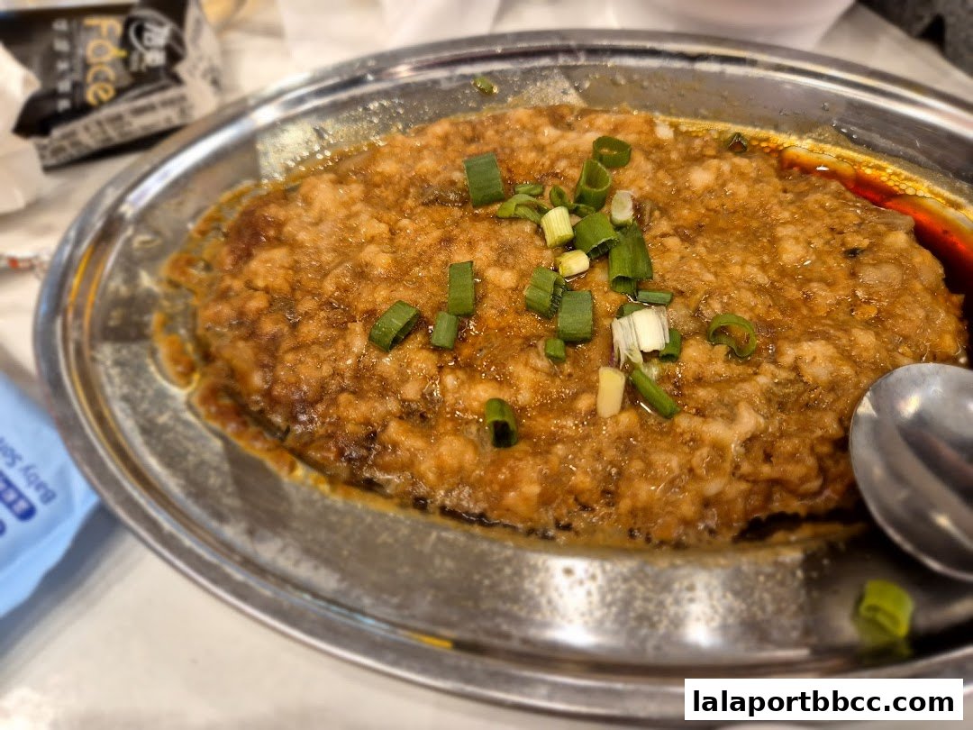 A close-up of a savory dish topped with chopped green onions in a metal serving dish.