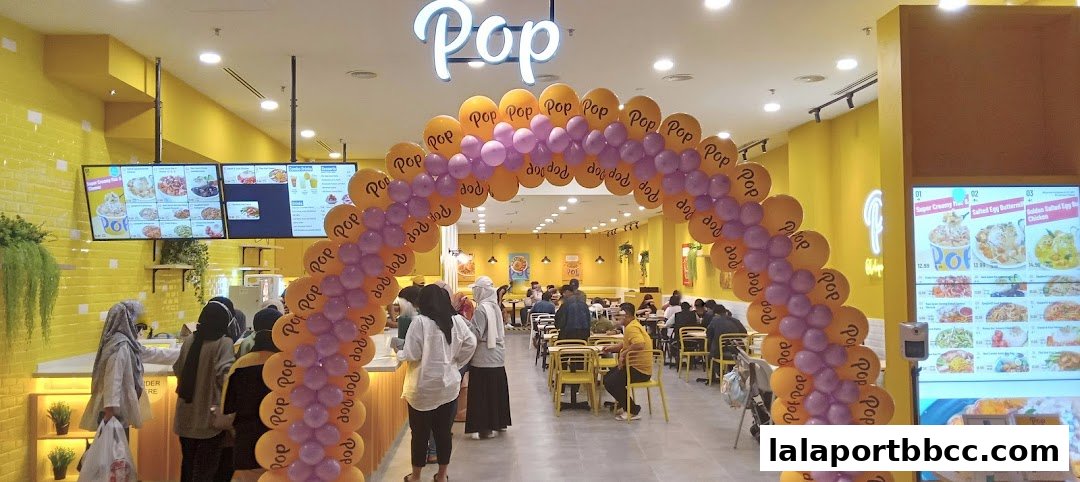 Interior of a brightly lit food hall with a balloon archway and customers ordering.