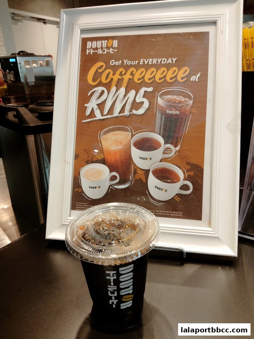 A cup of iced coffee sits in front of a framed advertisement for Doutor Coffee.