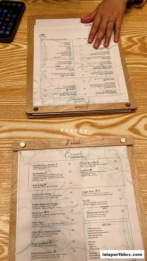 A person's hand rests on a menu at POKOK LaLaport, showcasing brunch options.
