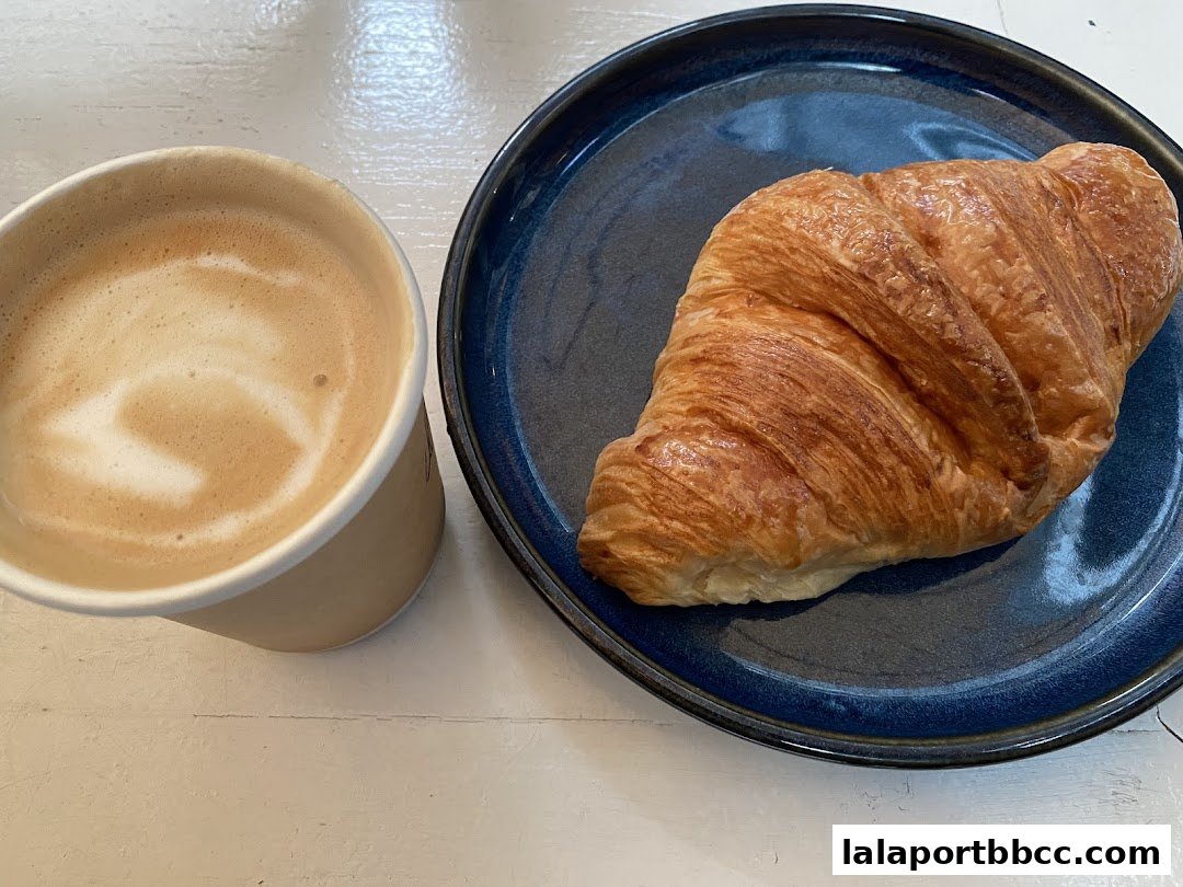 A close-up of a latte and a croissant on a blue plate.