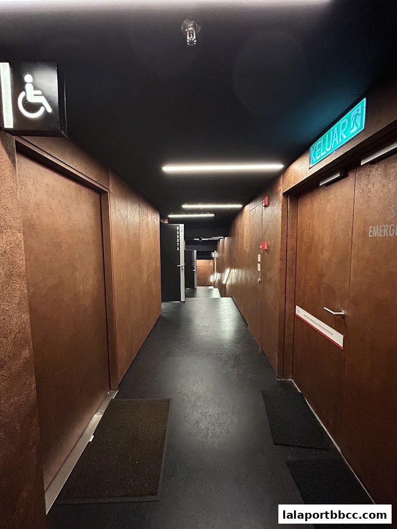 A modern hallway with brown textured walls, dark flooring, and illuminated signs.