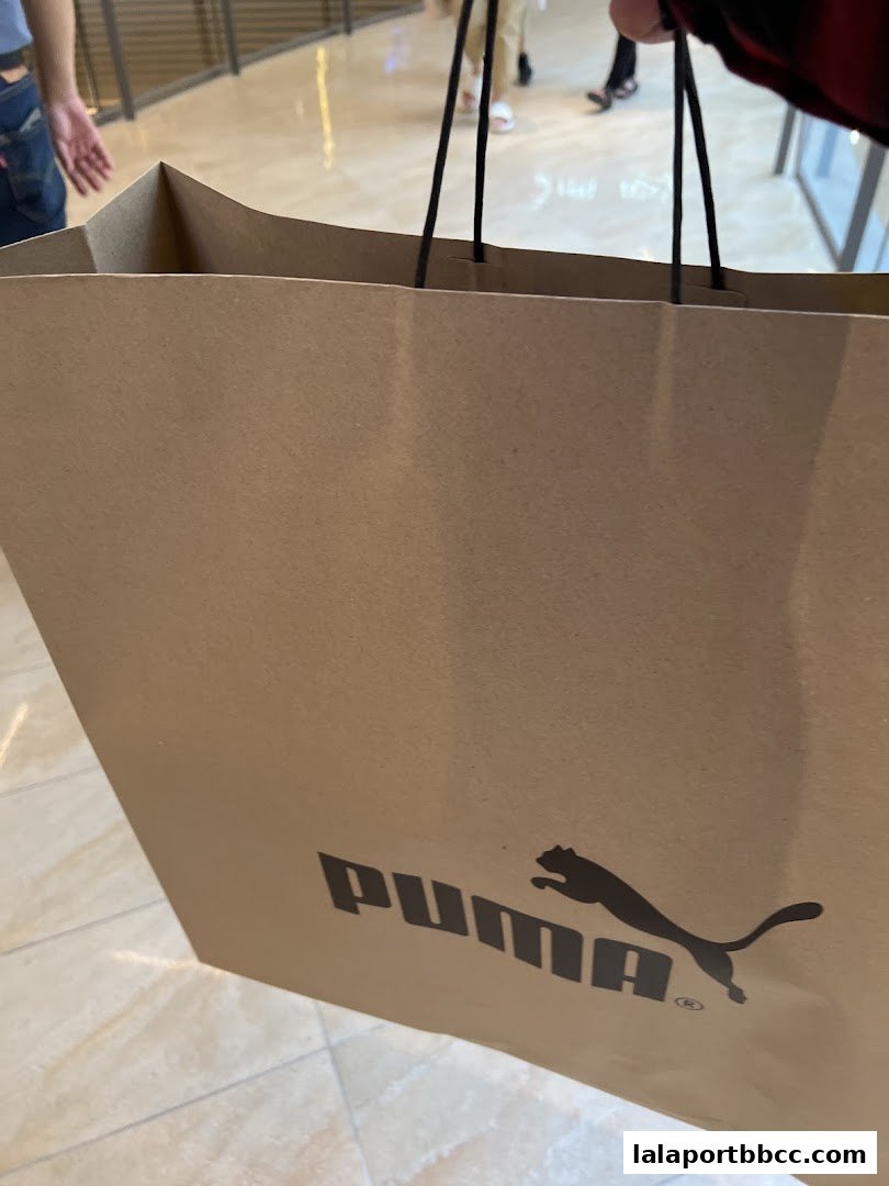 A person holds a brown PUMA shopping bag with the iconic leaping cat logo.