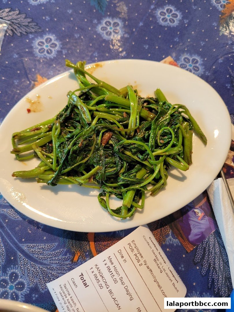 A plate of stir-fried kangkong served on a table with a receipt.