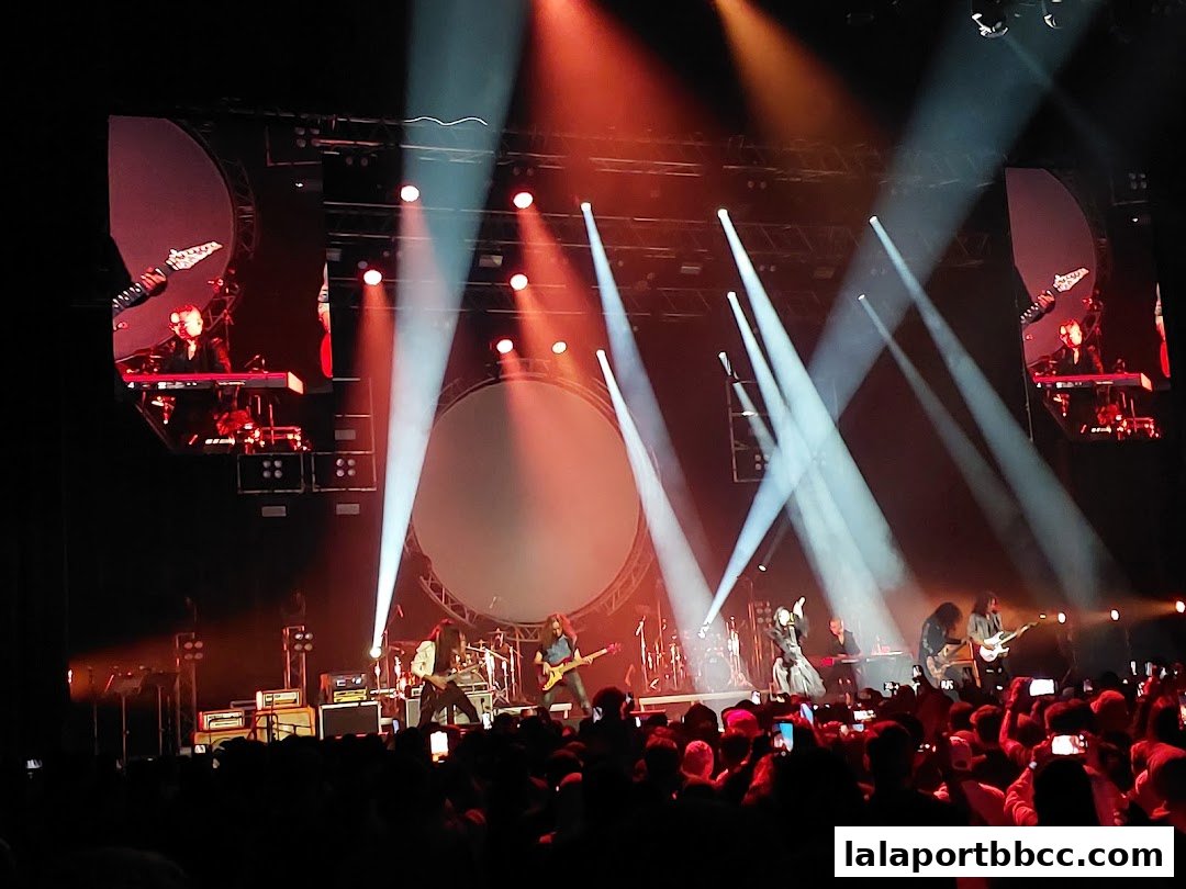 A live band performs on stage with dramatic lighting and a large circular screen.