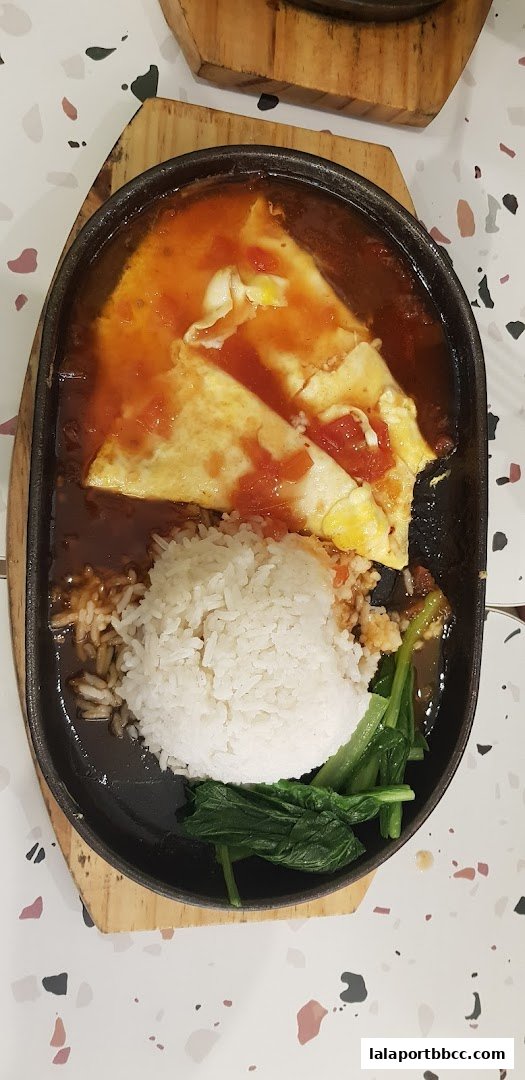 A sizzling claypot dish with rice, vegetables, and a tomato-based sauce with eggs.