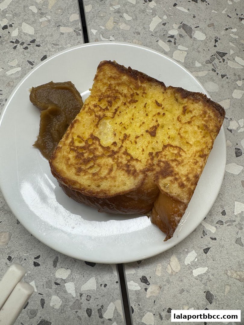 A close-up shot of golden-brown French toast served with a dollop of fruit compote on a white plate.