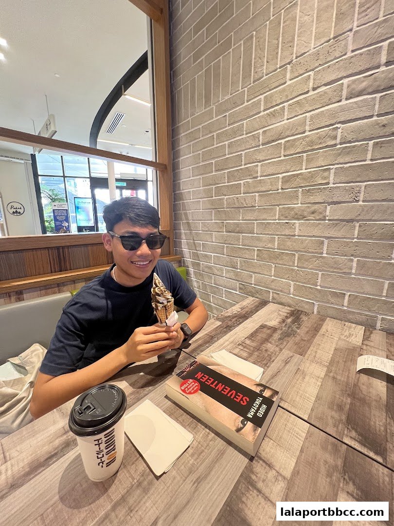 A young man enjoys a soft-serve ice cream cone and coffee at a table.