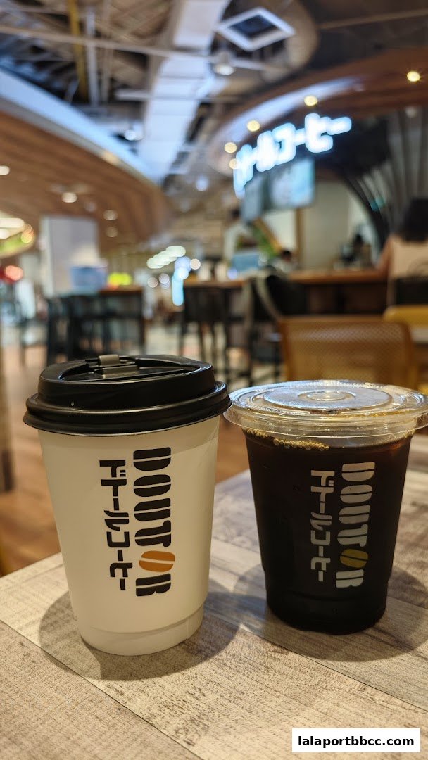 Two takeaway coffee cups from Doutor Coffee, one white and one black, sit on a wooden table.