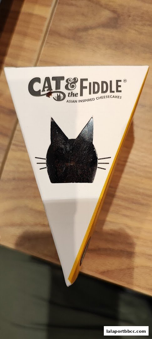 A triangular box with a black cat face design and the text 'CAT & FIDDLE ASIAN INSPIRED CHEESECAKES'.