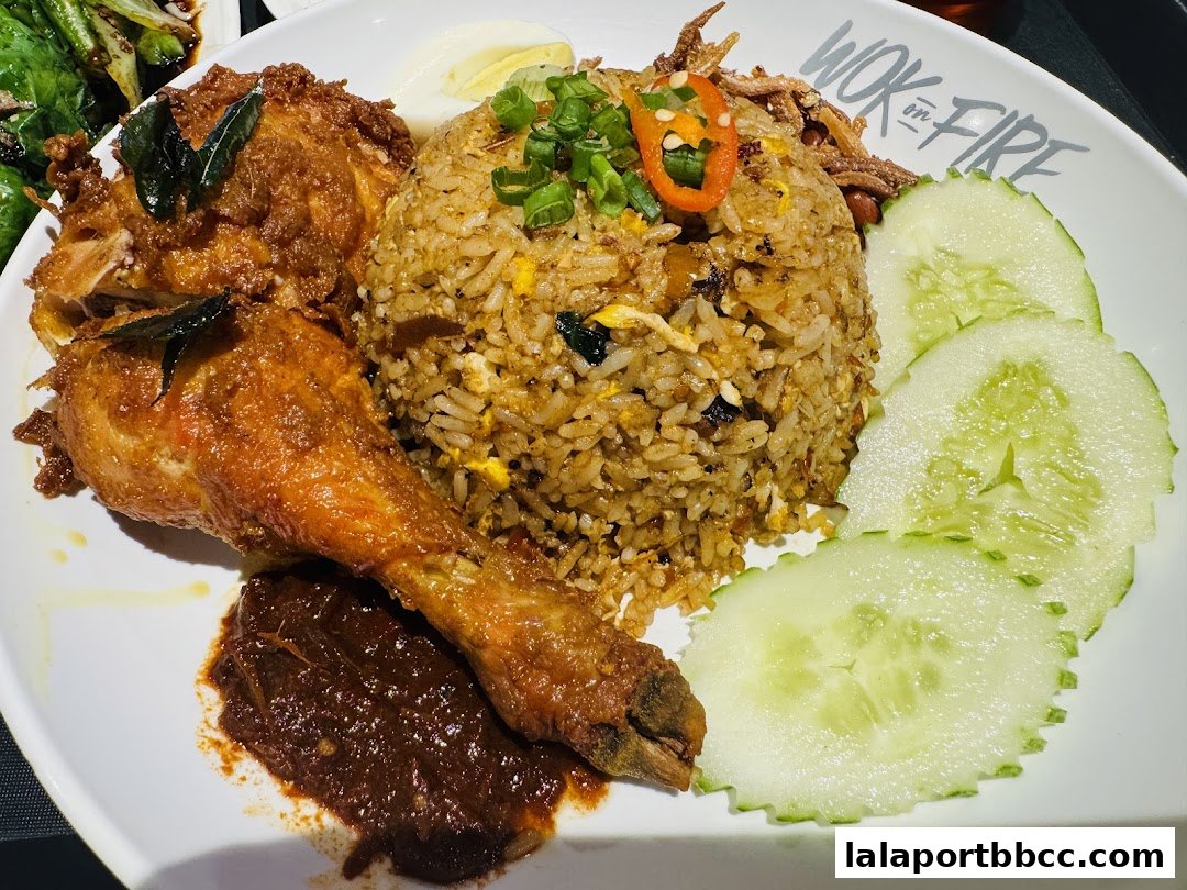 A plate of fried rice with crispy fried chicken, cucumber slices, and sambal.