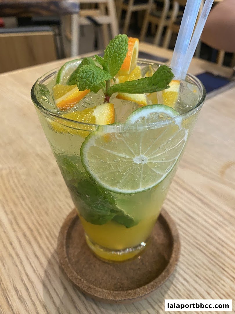 A refreshing citrus and mint beverage served in a tall glass with ice and fruit garnishes.