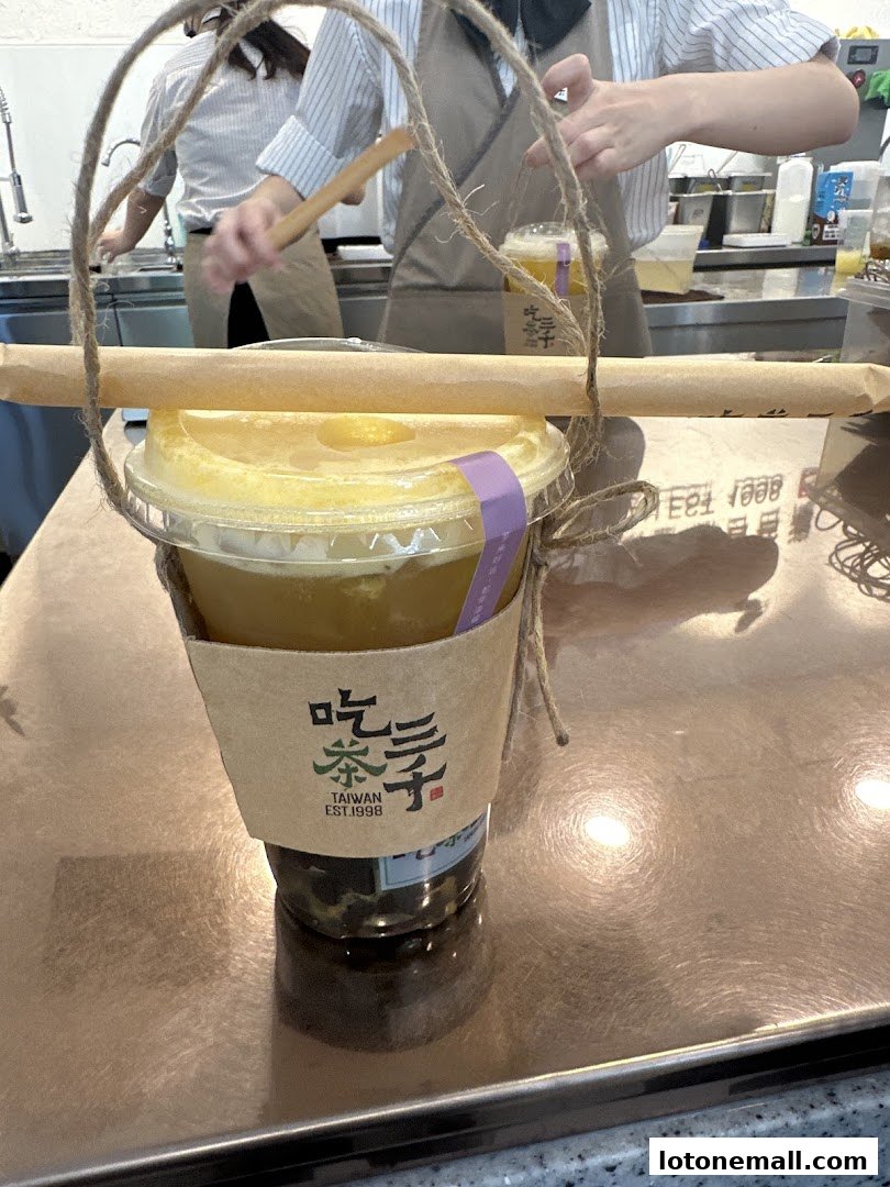 A takeaway bubble tea drink with a paper sleeve and twine handle, prepared by staff.