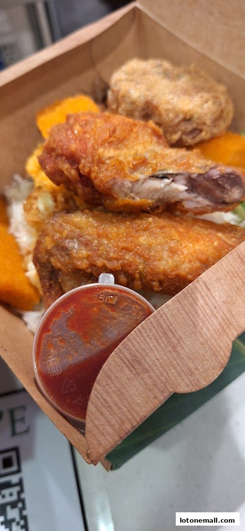 A close-up of a takeaway box filled with crispy fried chicken and other sides, with a small sauce container.