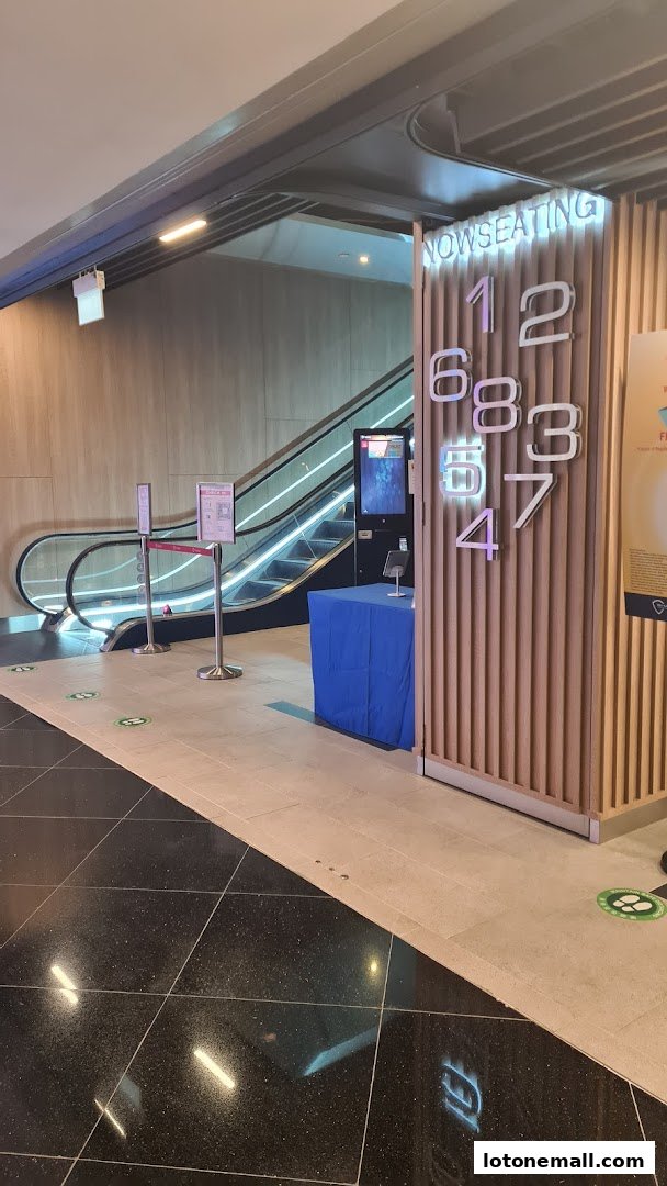 Entrance area with escalators, a digital kiosk, and decorative numbers on a wooden panel.