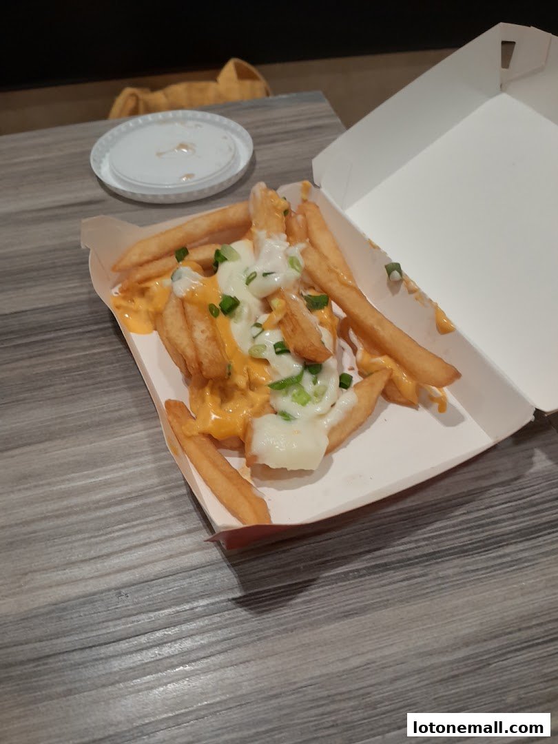 A box of cheesy fries topped with green onions on a wooden table.