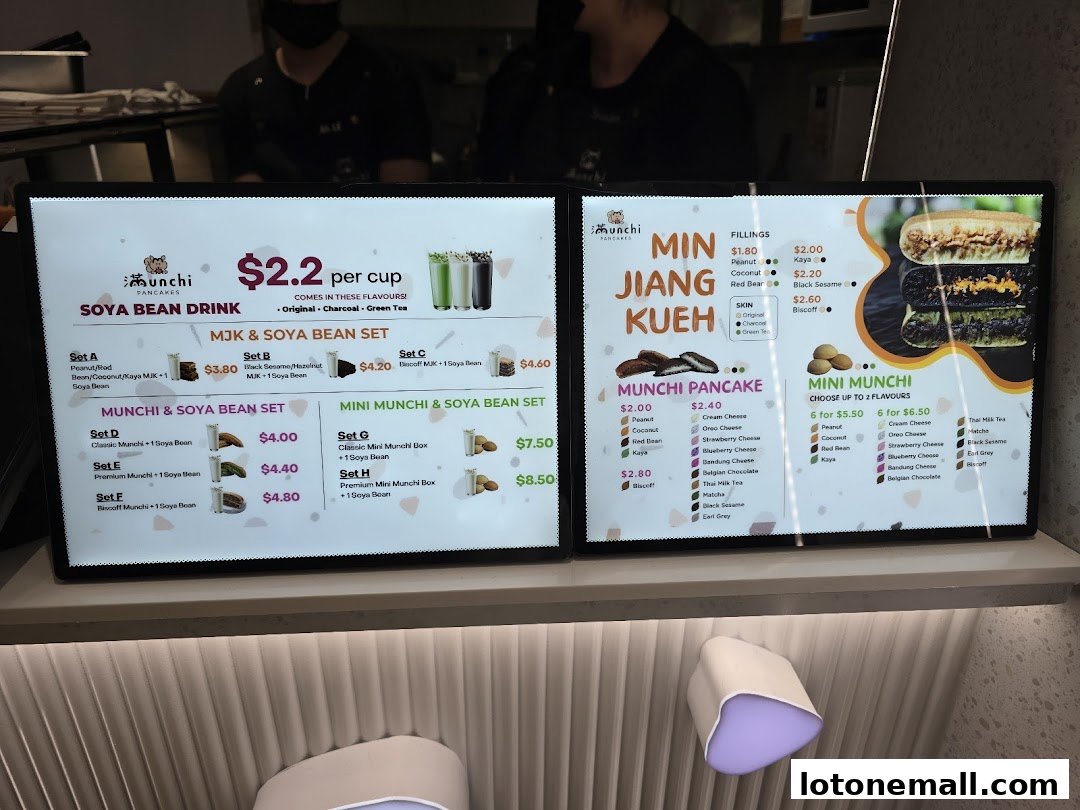 A digital menu board displaying Soya Bean Drinks, Min Jiang Kueh, and Munchi Pancakes with prices and flavors.