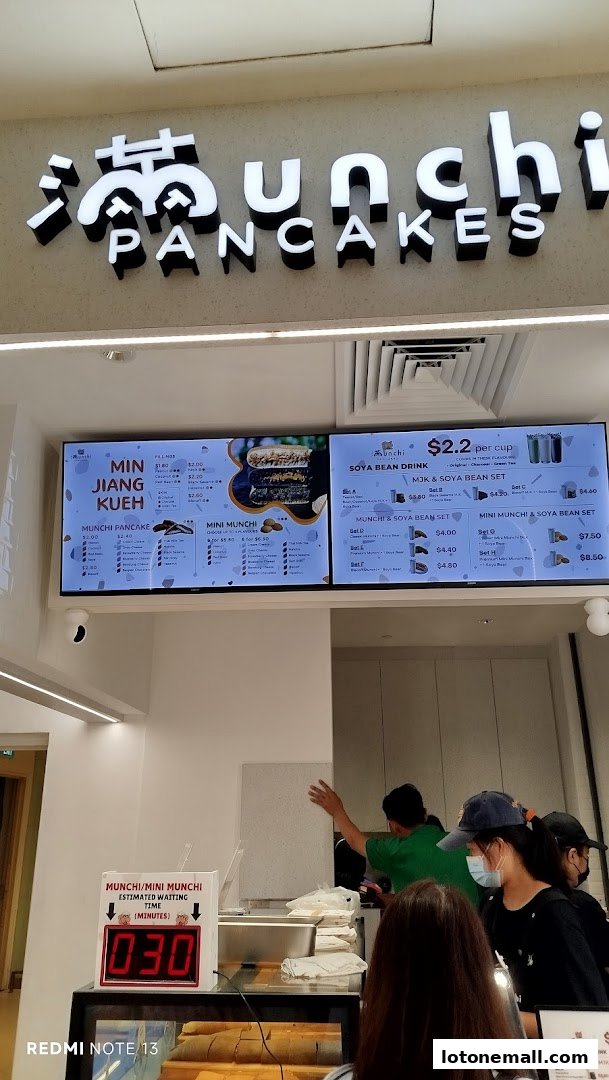 A digital menu board displays various pancake and drink options at Munchi Pancakes.