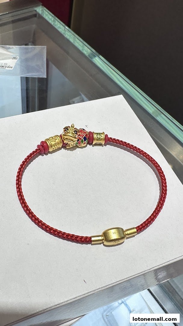 A close-up of a gold and red braided bracelet with a decorative frog charm.
