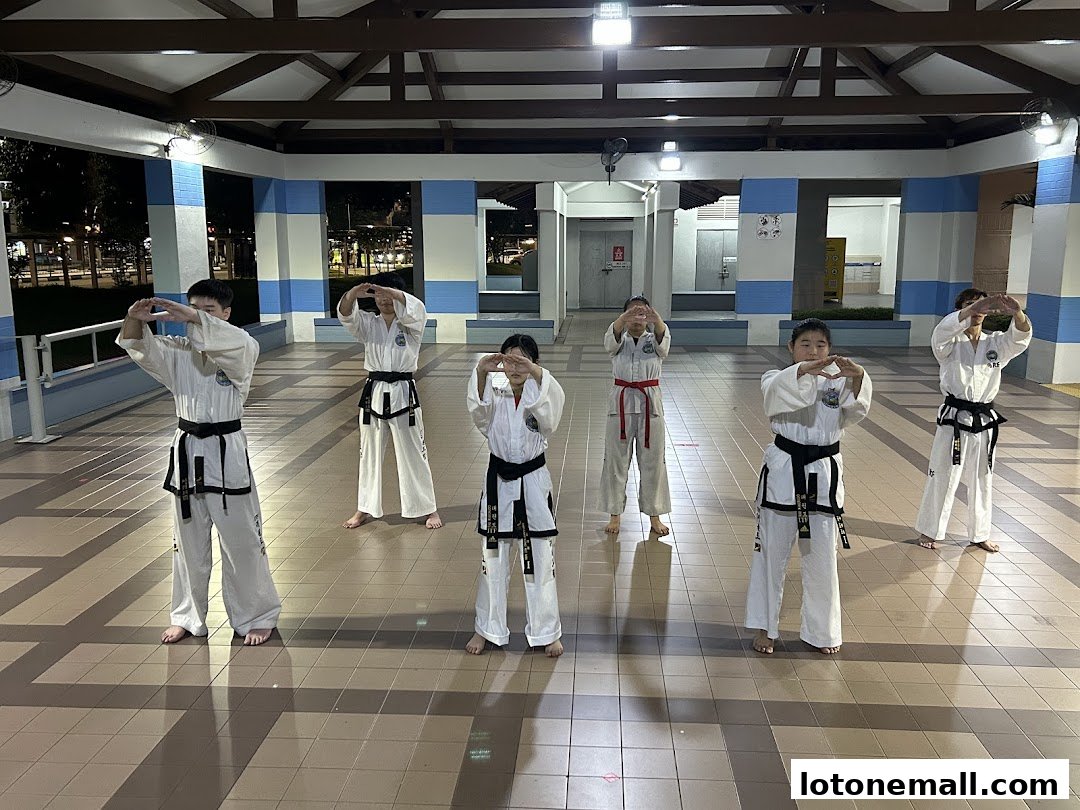 A group of children in Taekwondo uniforms practicing a stance outdoors.