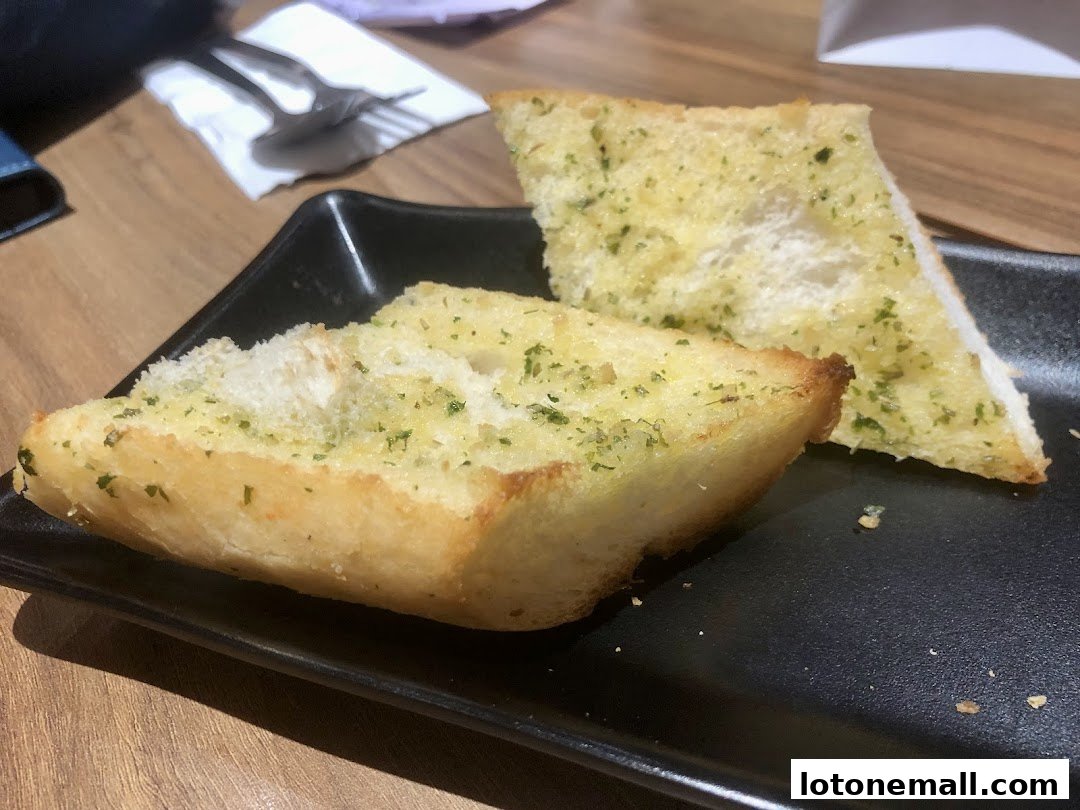 Two slices of garlic bread with herbs served on a black plate.