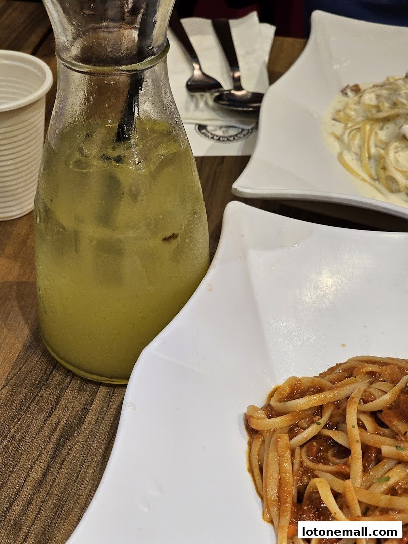 A refreshing drink and two plates of pasta on a wooden table.