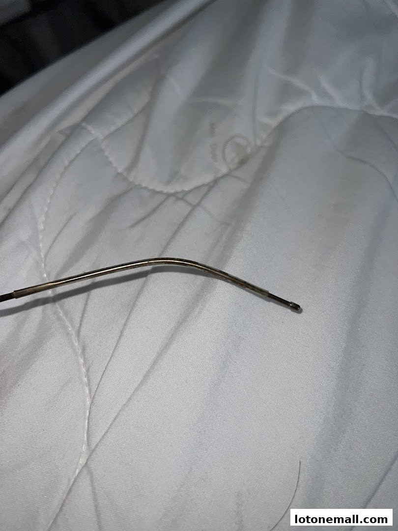 A close-up shot of a thin, metallic eyeglass arm resting on a white, quilted surface.