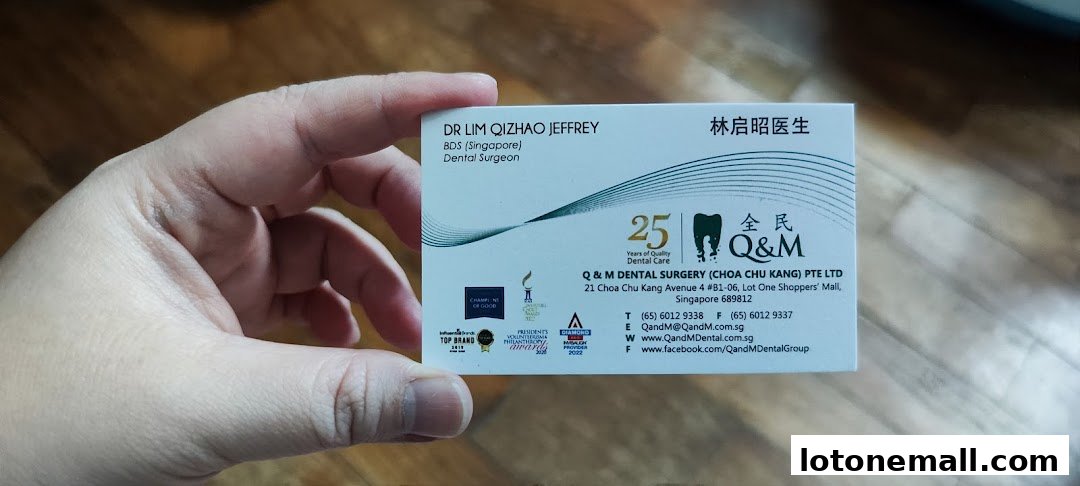 A business card for Q & M Dental Surgery, held by a hand.