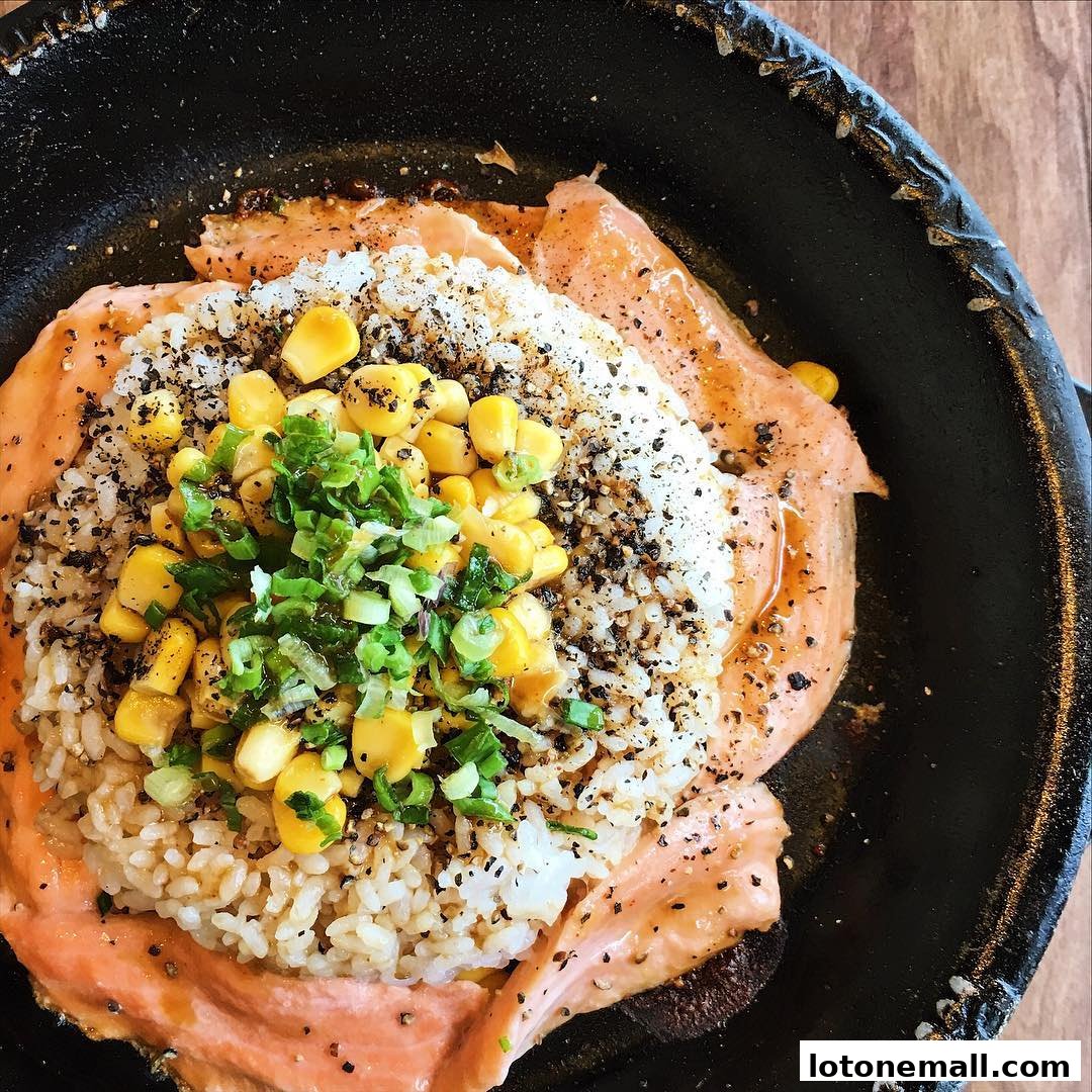 A sizzling hot plate of salmon, rice, corn, and scallions seasoned with pepper.