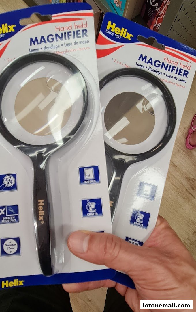Hands holding packaged Helix hand-held magnifiers with product details visible.