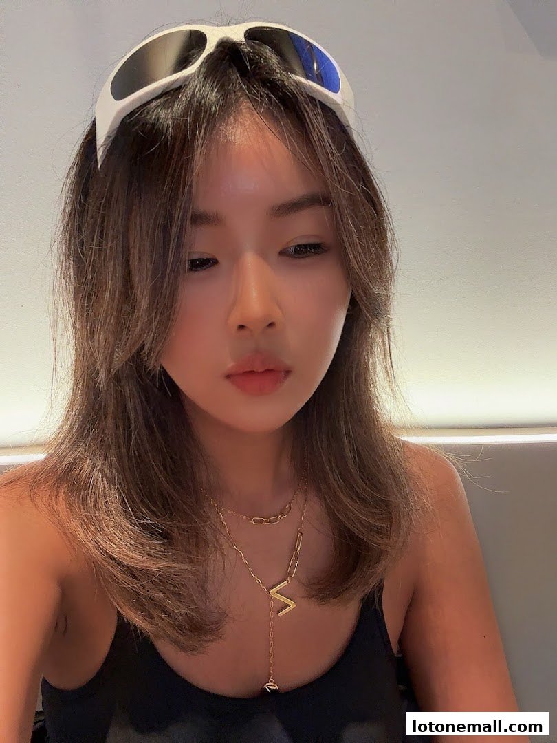 A young woman with stylish sunglasses and layered necklaces poses for a close-up shot.