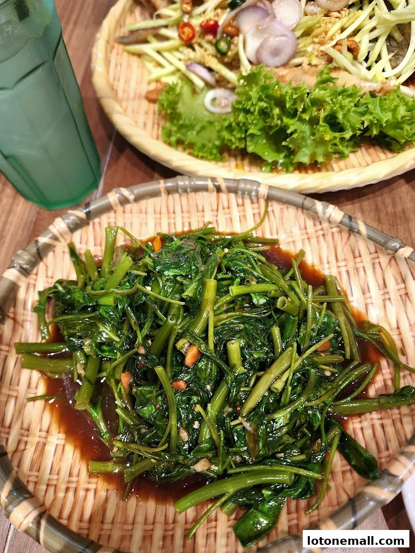A close-up of stir-fried water spinach with a side of salad and a drink.