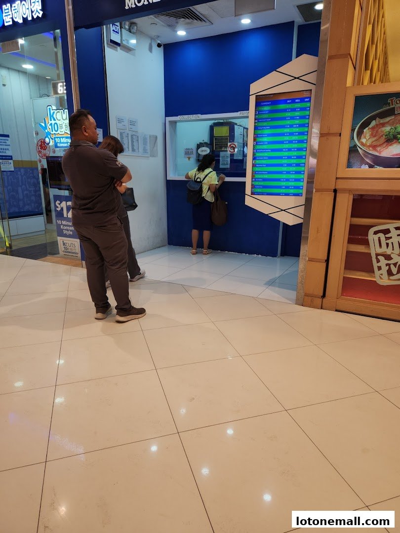 A money changer shop with customers at the counter and a digital display of exchange rates.