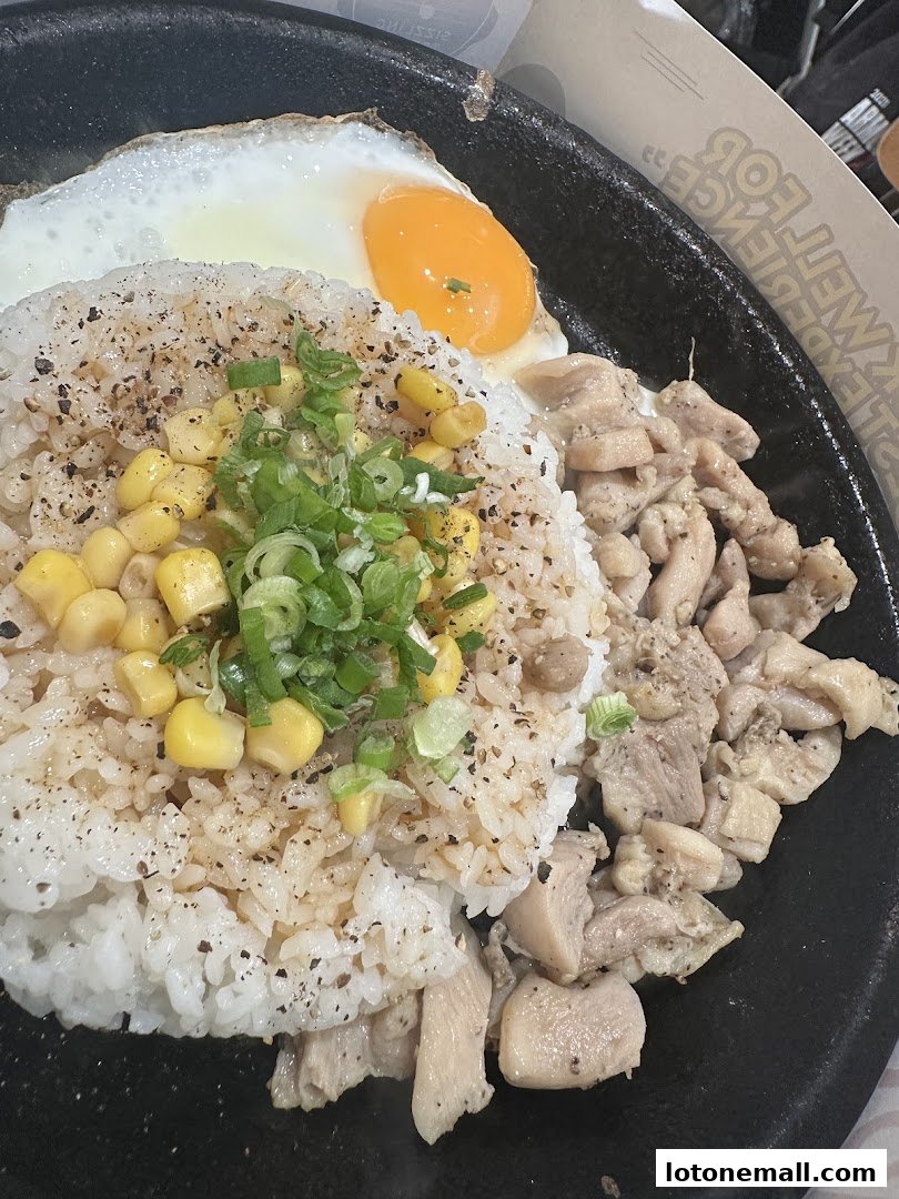 A sizzling hot plate of rice with chicken, corn, and a fried egg, seasoned with pepper and green onions.