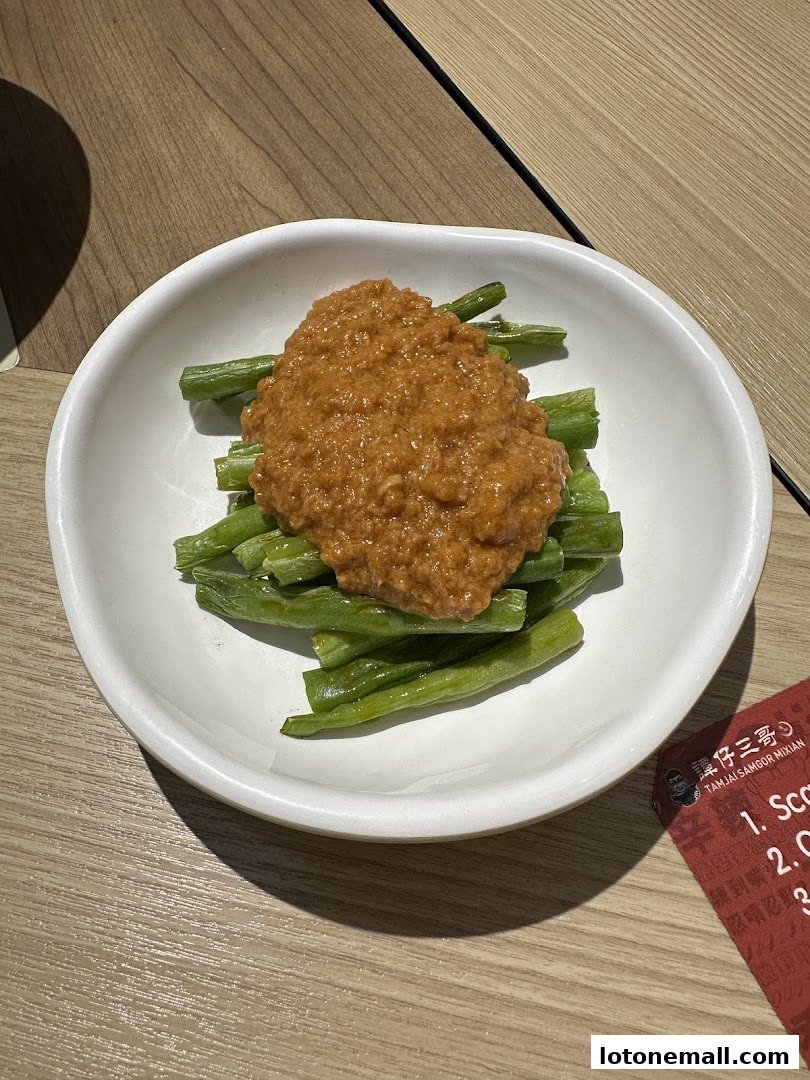 A white bowl filled with blanched green beans topped with a savory sauce.