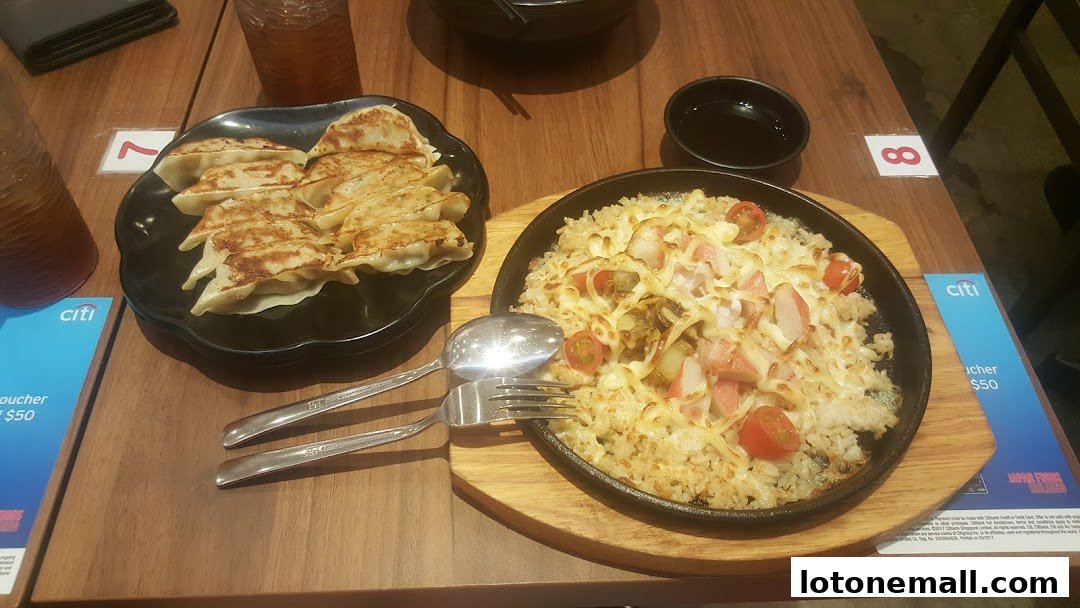 A table setting with a plate of gyoza and a sizzling dish of rice with seafood and cheese.