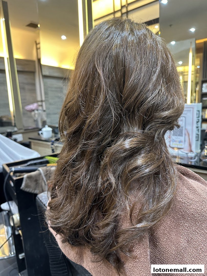 A person's back with styled, wavy brown hair in a salon.