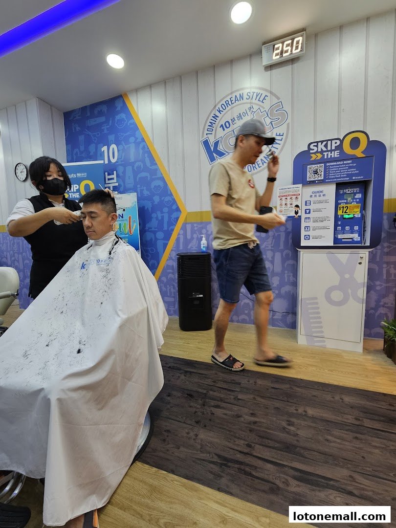 A barber is cutting a customer's hair while another person walks past a queueing machine.
