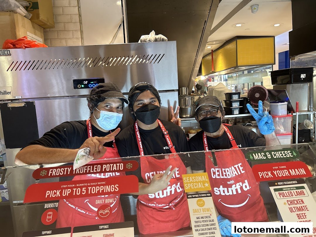 Three staff members wearing masks and aprons pose behind a counter at Stuff'd.