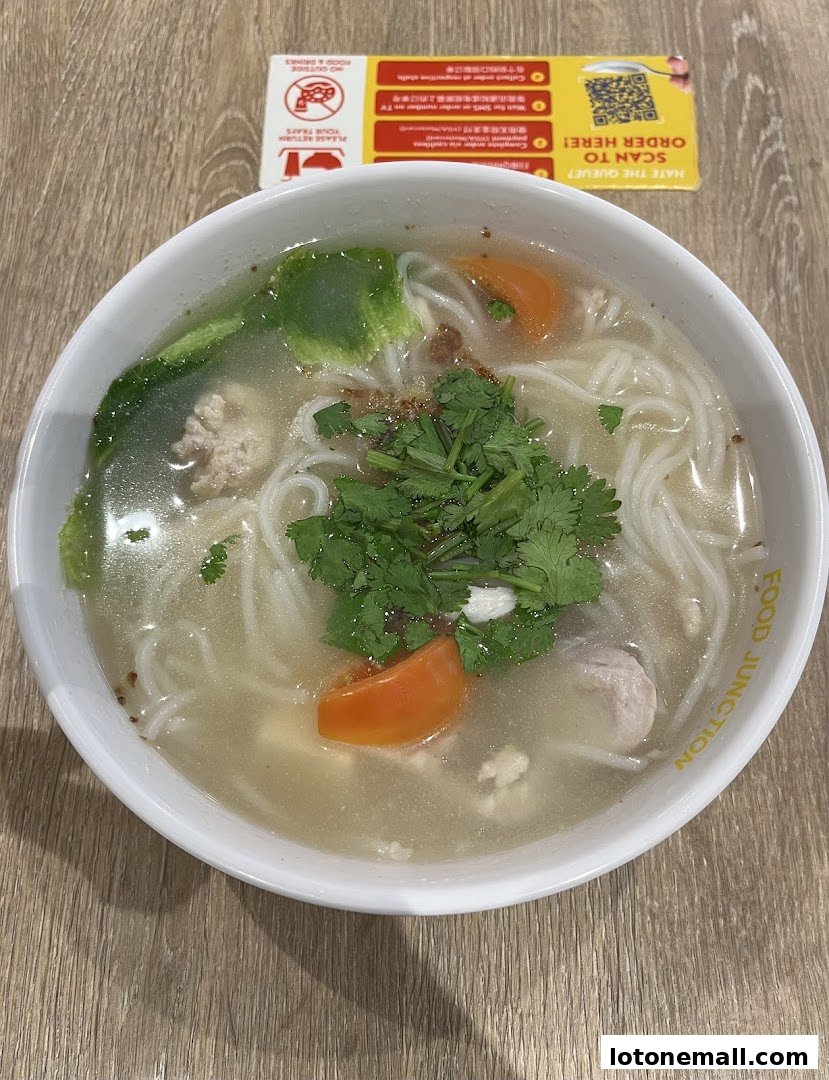 A bowl of noodle soup with meat, vegetables, and herbs from Food Junction.
